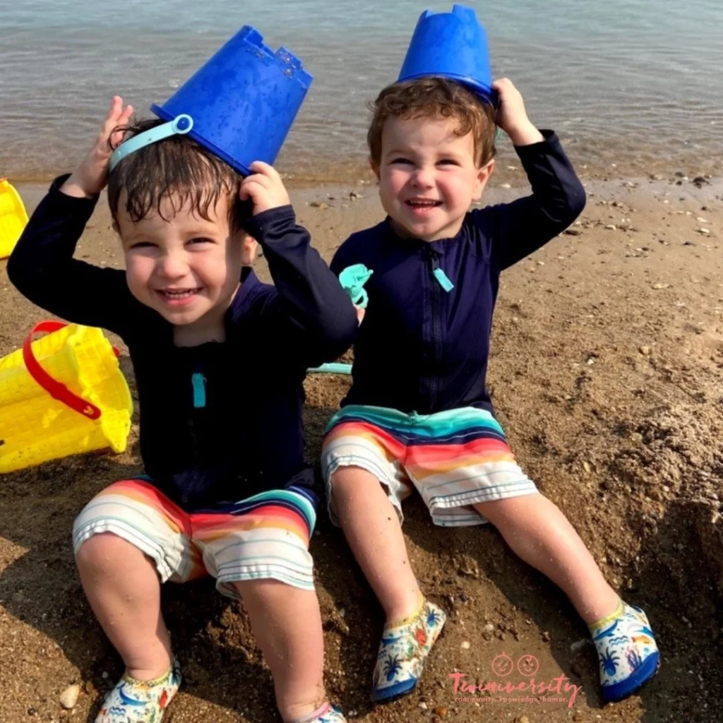 Twin boys playing in the sand at the beach wearing rash guards and swim shorts