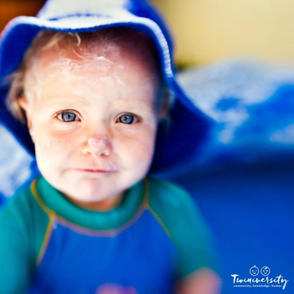 Baby boy wearing a blue swimsuit and sun hat with sunscreen all over his face