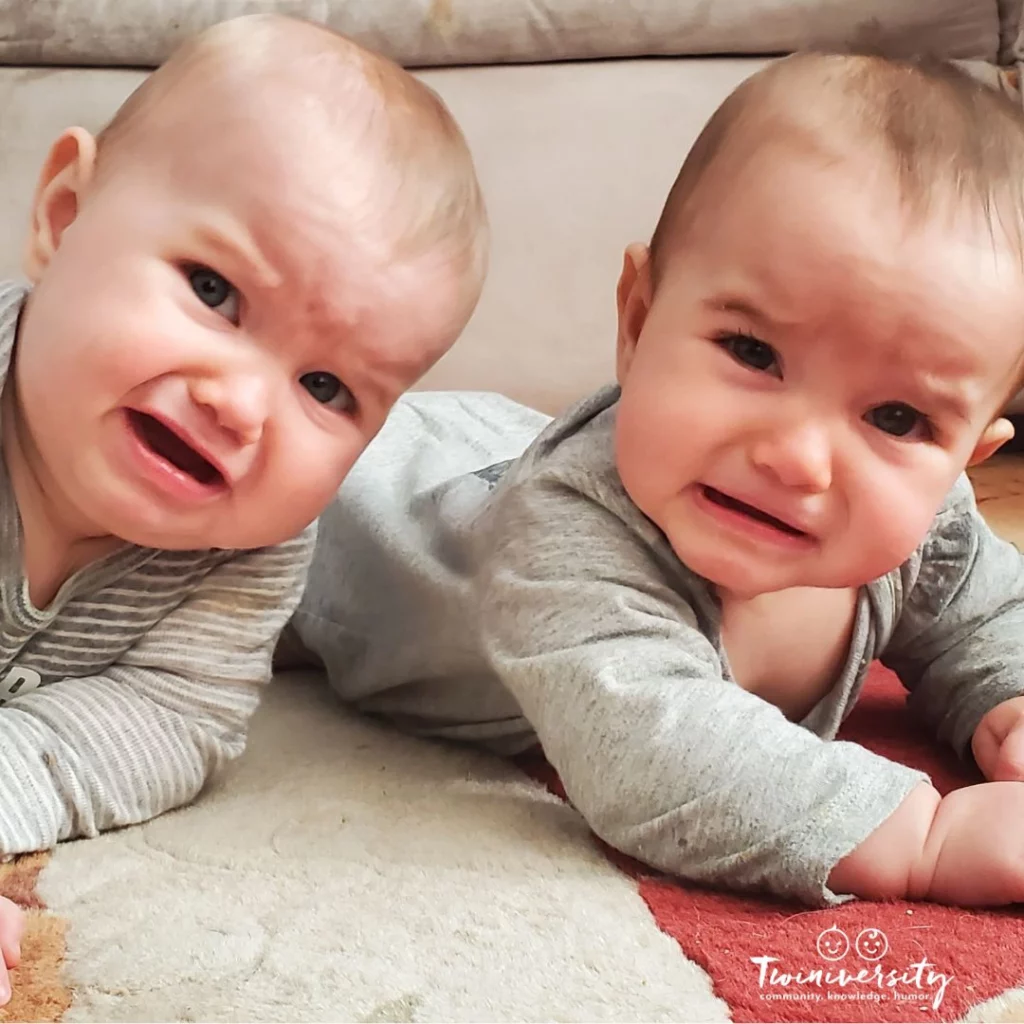 Two twin babies having tummy time and crying