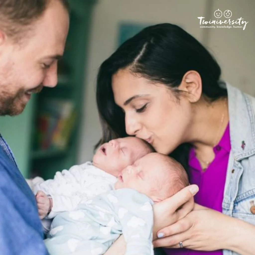 Dad holding both twin babies while mom kisses one on the forhead